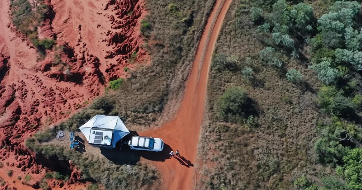 Aerial view of a 4WD and lightweight caravan set up on a red dirt Australian outback track