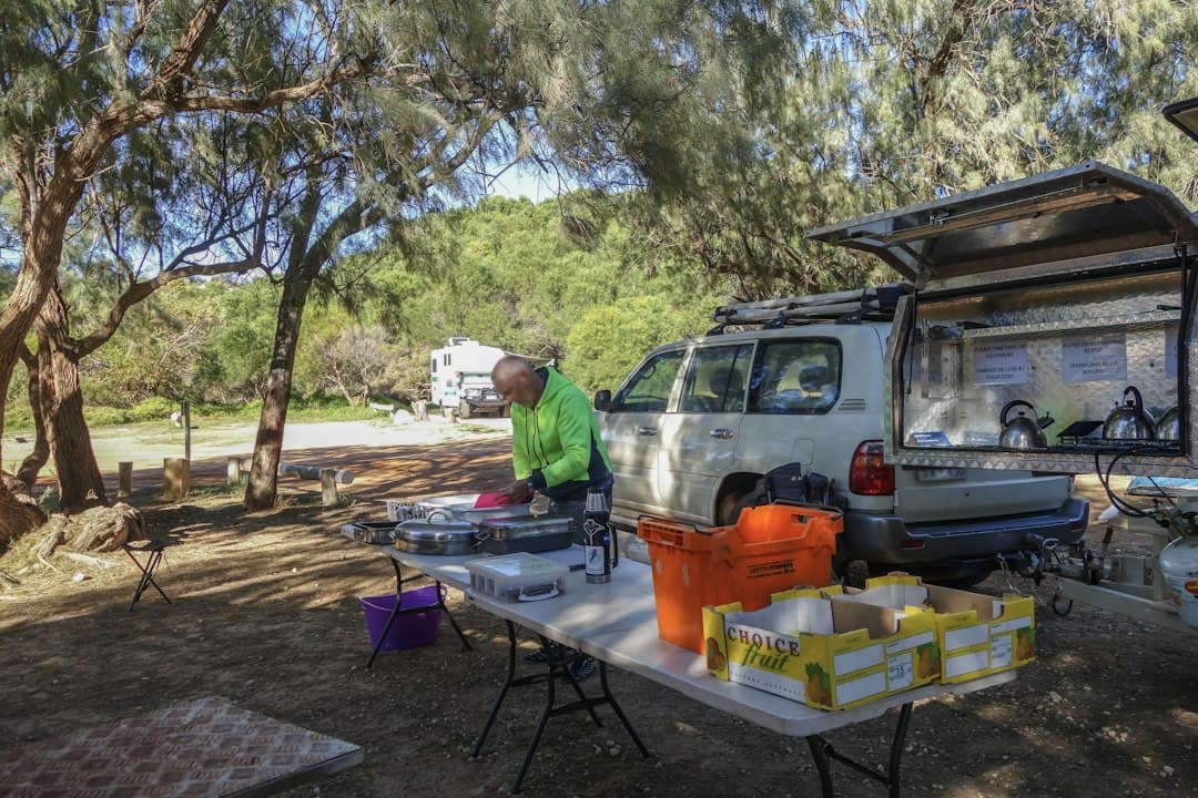 Camper sorting cooking gear and supplies on a folding table beside a 4WD and camper trailer kitchen